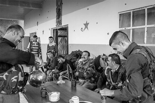 //A Kurdish YPG unit at their base on the front line in Ra's al-'Ayn. Right behind this building is the border with Turkey, so close that they can shout at the Turkish soldiers watching them. Al-Nusra Front snipers are also only 150 meters away. Photo by Younes Mohammad.